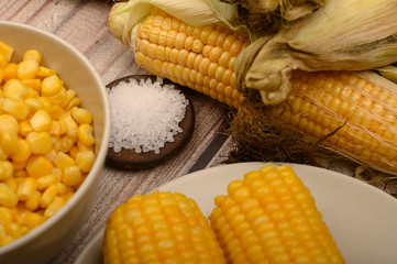 Two boiled ears of corn, corn kernels, coarse salt and raw ears of corn on a wooden table. Fitness diet. Healthy diet. For a sweet treat. Close up.
