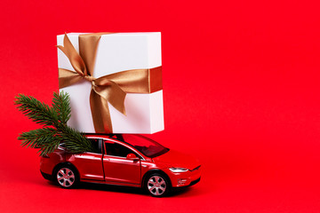 Christmas background. Red toy car with Christmas tree fir branch and present gift box on red background