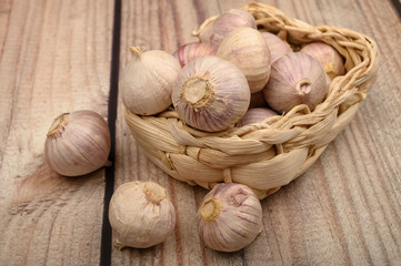 A few heads of young garlic in a wicker basket on a wooden background. Autumn harvest. Modern agriculture. Close up.