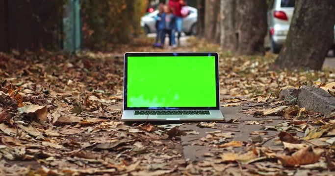 Green screen laptop with romantic fiery autumn city and walking children on background. Free mock up content. Chroma-key notebook display. Freelance business app. Social networking. Online shopping.