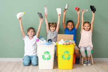 Little children and containers with trash near color wall. Concept of recycling