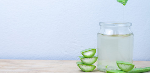 Fresh aloe vera leaves and a glass of aloe vera juice on a wooden table.