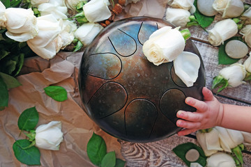 The Handpan is traditional ethnic drum musical instrument with roses background near the child's hand.