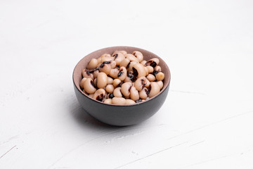 Cooked Fradinho beans in a black clay pot, isolated on a white background.