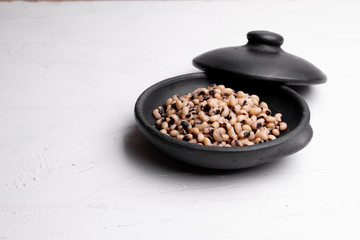 Cooked Fradinho beans in a black clay pot, isolated on a white background.