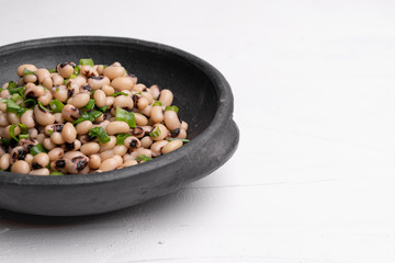 Cooked Fradinho beans in a black clay pot, isolated on a white background.
