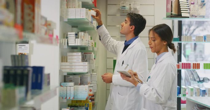 The young pharmacists consultants are checking with a tablet medicines on the shelf of drug store. 