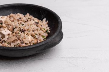Baião de Dois - Brazilian Traditional Food - made with sausage, curd cheese, dried beef and rice in a black clay pot, on white background. Typical dish of Northeast Brazil.