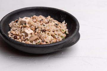 Baião de Dois - Brazilian Traditional Food - made with sausage, curd cheese, dried beef and rice in a black clay pot, on white background. Typical dish of Northeast Brazil.