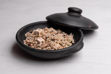 Baião de Dois - Brazilian Traditional Food - made with sausage, curd cheese, dried beef and rice in a black clay pot, on white background. Typical dish of Northeast Brazil.