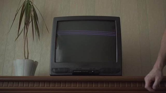 man switches on TV set and chooses channels on broken device with rippling screen against beige wall closeup