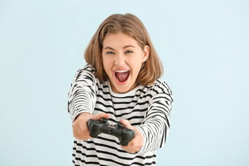 Emotional teenager girl with game pad on light background © Pixel-Shot