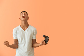 Emotional African-American teenager boy with game pad on color background - obrazy, fototapety, plakaty