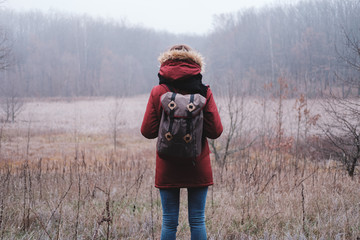 Hiker woman with backpack walking in the autumn forest on a foggy cold day.  Concept of travel lifestyle, vacations outdoor. Travel alone into the wild