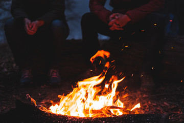 Two people sit by the bright bonfire at dusk. Spending nice time outdoors in chilly weather at a camping place - tranquil and peaceful scene © Photoboyko