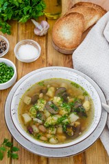 Soup with beans, mushrooms and dumplings in a bowl on a dark wooden background with herbs and garlic. Vegan (lean) dish. Rustic style.