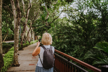 Traveler elderly senior backpacker woman  walking taking photos in tropical park, Travel adventure nature in China, Tourist beautiful destination Asia, Summer holiday vacation trip, Copy space