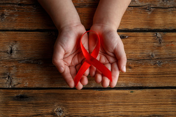 Red ribbon in children's hands on a dark wooden background, a symbol of the fight against HIV, AIDS and cancer. The concept of helping the needy.