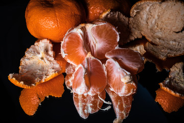 Fresh organic tangerines, whole and sliced, with reflection on shiny black background