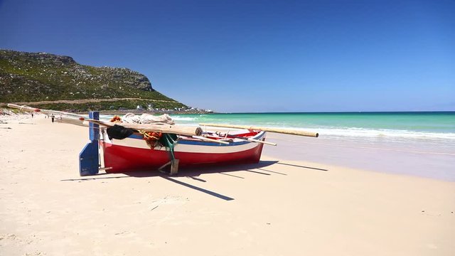 Small traditional type of fishing row boat resting on sand on Fish Hoek Beach, Cape Town
