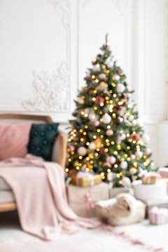 Blured photo of decorated wit garland and toys christmas tree standing next to white sofa.