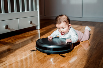 A baby with a robotic vacuum cleaner on the floor