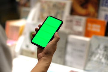 over shoulder view of man holding green screen phone in book store. blurred books as background