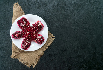  Pomegranate in a white plate on a black background. Flat lay. Copy space.