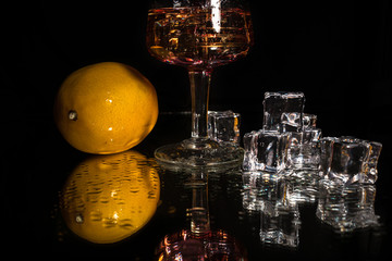 Alcohol drink in a glass whole lemon and ice cubes with reflection on shiny black background