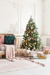 Christmas tree decorated by garland and gift boxes stands close to sofa