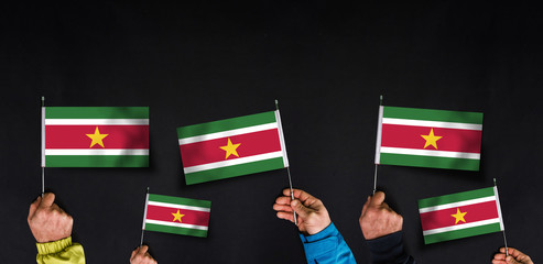 Fototapeta na wymiar Hands holds flags of Suriname on dark background