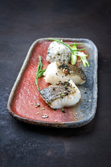 Gourmet fried Japanese skrei cod fish filet with glasswort and furikake onigiri as closeup on a modern design plate