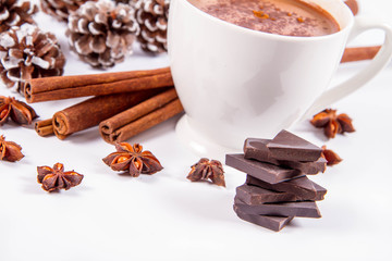 Cup of hot chocolate with cinnamon, anise stars, pieces of dark chocolate and some cones	