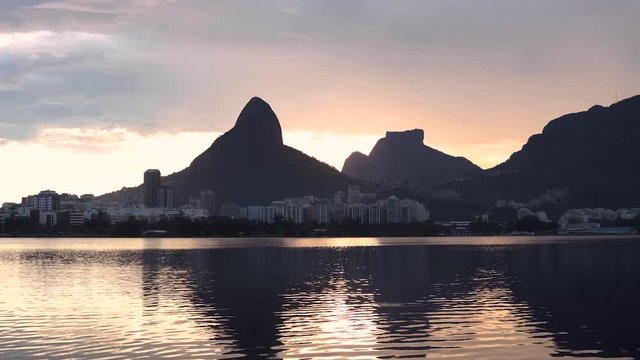 Time lapse of sunset at city lake in Rio de Janeiro setting behind the Two Brothers and Gavea mountain with their reflection in the water in the foreground