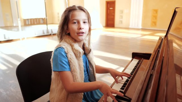 A young beautiful girl plays the piano and sings cheerfully cheerfully. Music lessons.