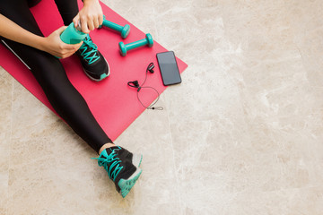 Stock photo of a young woman resting after exercising at home in the living room with a bottle