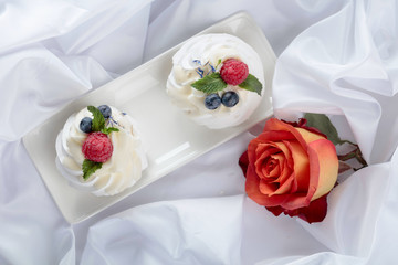 Dessert Pavlova with raspberries, blueberries and mint on a white fabric.