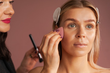 Close up working process Makeup artist applies skin tone with Sponge makeup egg. Beautiful woman's face. Professional makeup lessons