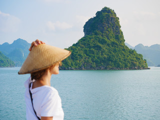 Woman with traditional looking at unique view of Halong Bay, Vietnam. Tourist traveling on cruise among Ha Long Bay rock pinnacles in the sea. Caucasian lady having fun on vacation to famous landmark.