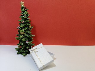 small christmas tree with white gift box on white surface and red background