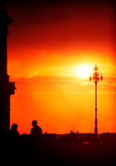 Red sky at sunset over the sea promenade and Unita' d'Italia square at Trieste, Italy with silhouettes of a building and people in back light
