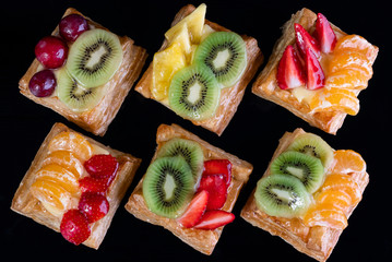 puff pastry with tangerine, kiwi and strawberry fruit on black background viewed from above