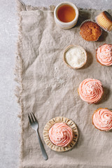 Homemade cupcakes with pink buttercream and coconut flakes served with ceramic cup of tea over grey linen cloth as background. Flat lay, space