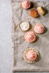 Fototapeta na wymiar Homemade cupcakes with pink buttercream and coconut flakes served on ceramic plate over grey linen cloth as background. Flat lay, space