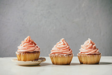 Homemade cupcakes with pink buttercream and coconut flakes in row on white marble table. Copy space.