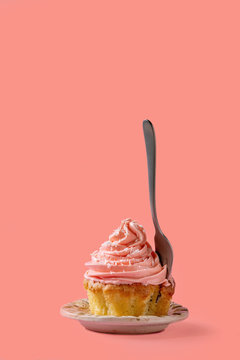 Homemade cupcake with pink buttercream and coconut flakes, with dessert fork within over red pink background.
