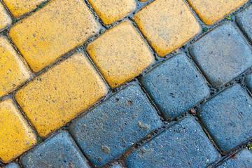 yellow and blue cobbles of pavement texture. stone masonry floor covering close up. top view of wet diagonal grungy background