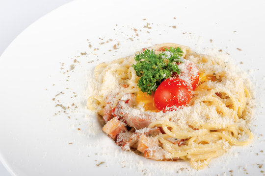typical spaghetti alla carbonara  with raw egg and bacon. served on a white plate with grated Pecorino cheese. decorated with cherry tomato and parsley. side view