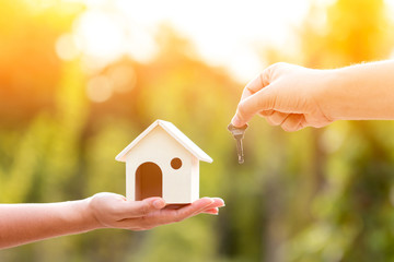 Buying a new house concept, a women and man hand holding a model home and a key put together in the public park.