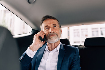 Senior businessman making phone call while sitting on back seat of a car